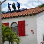Do termite treatment services require home preparation before arrival - Workers inspecting roof of white house with red door.