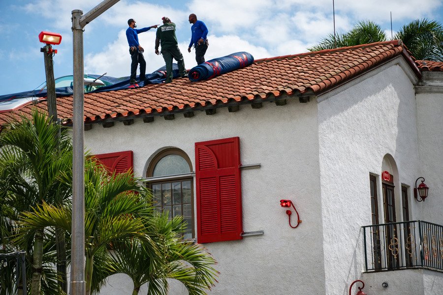 Do termite treatment services require home preparation before arrival - Workers inspecting roof of white house with red door.
