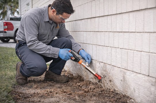 Termite Treatment & Pest Control Application - Technician injecting termite treatment along foundation.