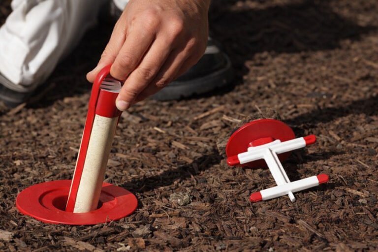 Fast termite treatment - Hand placing a red termite bait station into soil with tool beside it.