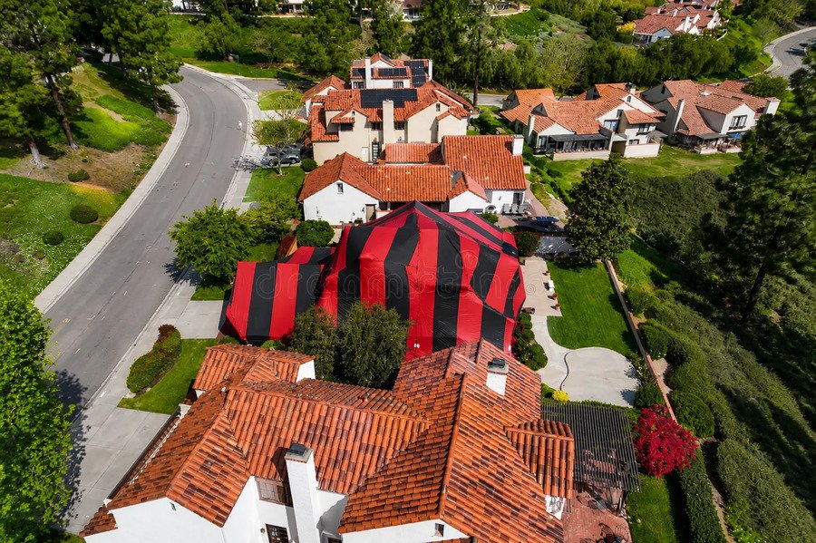 House covered with red and black fumigation tent in suburban neighborhood